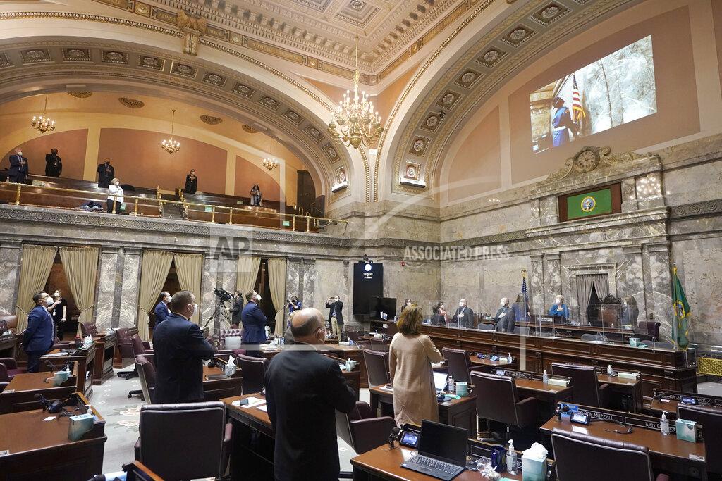 Ted S. Warren FILE - In this Jan. 11, 2021 file photo, Washington state senators stand as a ceremonial presentation of colors is shown on a video display on the first day of the 2021 legislative session at the Capitol in Olympia, Wash. The 2021 session of the Washington Legislature ended Sunday, April 25 and lawmakers had no shortage of weighty topics to consider while having to conduct their work amid a pandemic that meant most meetings and votes were conducted remotely. The Capitol building was also closed to the public since last year due to the COVID-19 pandemic, and was surrounded by security fencing and national guard members at times due to fears of protests. (AP Photo/Ted S. Warren, File)