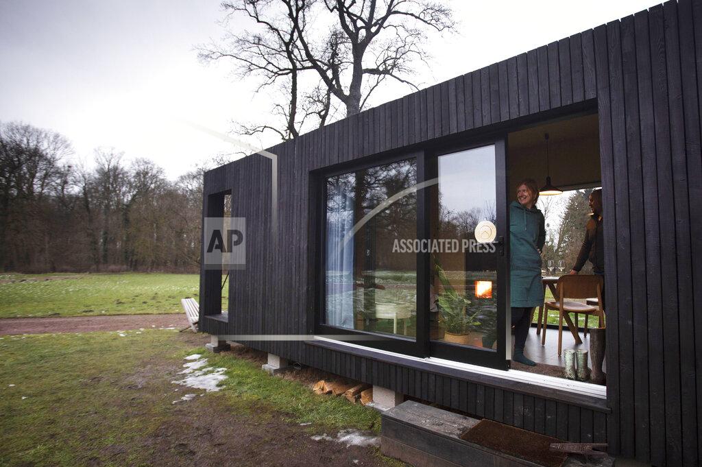 Virginia Mayo Kim Devos, from Erpe, Belgium looks out the sliding door of a Slow Cabin in Elewijt, Belgium, Monday, Feb. 15, 2021. These Slow Cabins, set up the Belgian countryside, are the new way to vacation in pandemic times: in complete solitude and in the middle of nowhere. The wooden cabins are fully sustainable, provided you don't stay in the shower too long and you can live without Wi-Fi. (AP Photo/Virginia Mayo)