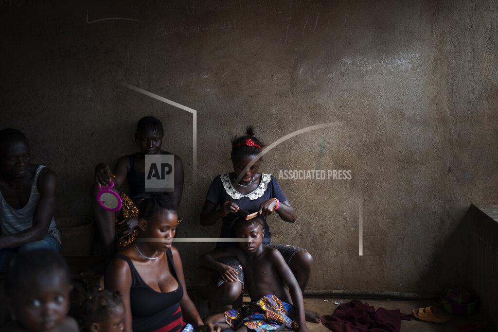 Leo Correa A woman combs the hair of a girl as they watch a video clip on a portable DVD player in Komao village, on the outskirts of Koidu, district of Kono, Sierra Leone, Sunday, Nov. 22, 2020. (AP Photo/Leo Correa)