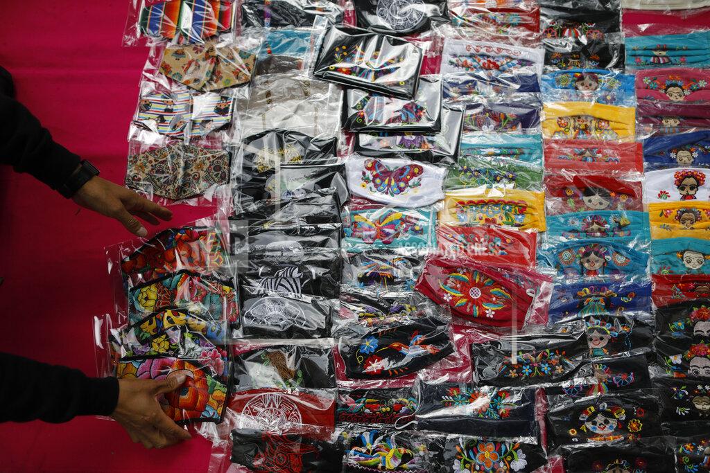 Rebecca Blackwell FILE - In this Aug. 17, 2020 file photo, Luis Fuentes, 45, from Ecuador, gathers up face masks decorated with traditional Mexican designs, as he puts away his wares as it begins to rain, on Insurgentes Avenue in Mexico City. According to a report released the third week of April, by the University of California, San Francisco, Mexico would have had a significantly lower COVID-19 death toll if it had reacted as well as the average government. (AP Photo/Rebecca Blackwell, File)