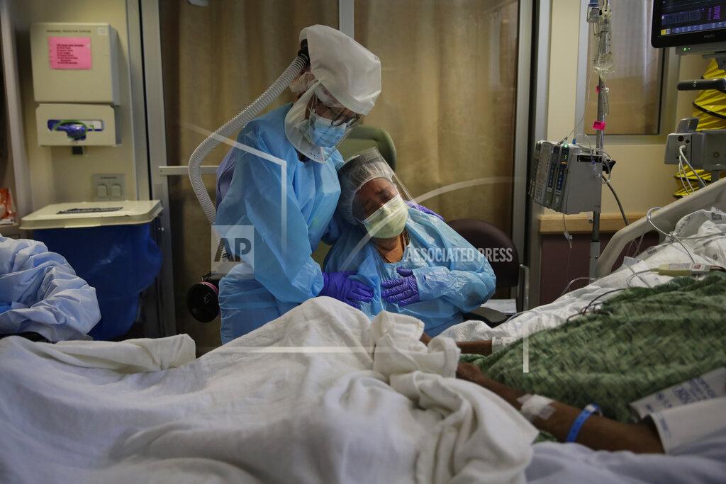 Jae C. Hong FILE - In this July 31, 2020, file photo, Romelia Navarro, right, is comforted by nurse Michele Younkin as she weeps while sitting at the bedside of her dying husband, Antonio, in St. Jude Medical Center's COVID-19 unit in Fullerton, Calif. The U.S. death toll from the coronavirus topped 200,000 Tuesday, Sept. 22, a figure unimaginable eight months ago when the scourge first reached the world’s richest nation with its sparkling laboratories, top-flight scientists and towering stockpiles of medicines and emergency supplies. (AP Photo/Jae C. Hong, File)