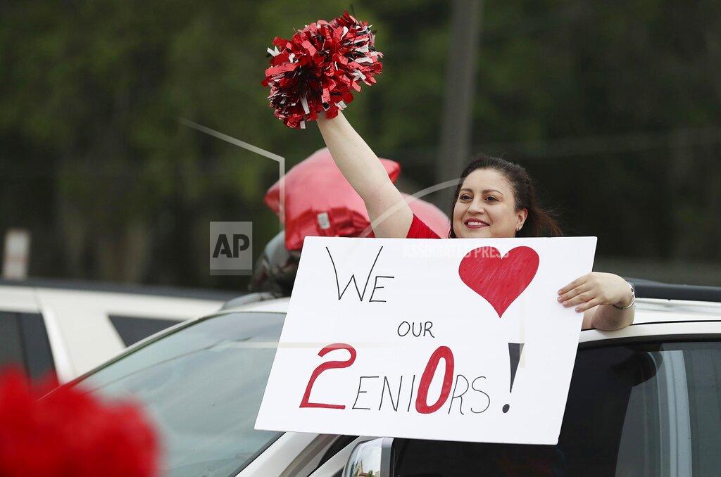 Limor Moake, a Spanish teacher at Tavares High, cheers as graduating seniors receive their cap and gowns during a parking lot pep rally at Tavares High School on Monday, April 20, 2020. While practicing social distancing, seniors came to campus to drive through to pick up their caps and gowns from their cars. With proms canceled and graduation ceremonies postponed, parents, teachers and others are looking for opportunities to celebrate the Class of 2020 despite the global pandemic that has the state under a stay-at-home order. So, what could have been a routine distribution of caps and gowns to Lake County high school seniors, became a parking lot pep rally. (Stephen M. Dowell/Orlando Sentinel via AP)