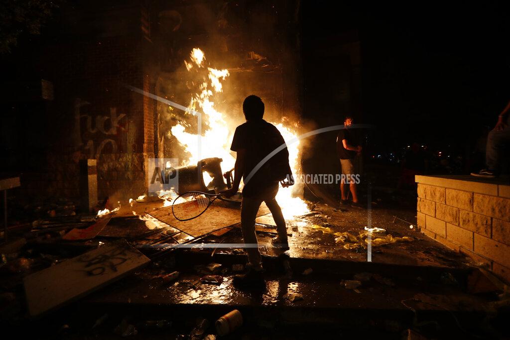 John Minchillo EDS NOTE: OBSCENITY - Protesters add fuel to a fire at the Minneapolis police 3rd Precinct building Thursday, May 28, 2020, in Minneapolis. Violent protests over the death of George Floyd, a black man who died in police custody Monday, broke out in Minneapolis for a third straight night. (AP Photo/John Minchillo)