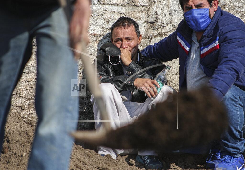 Esteban Felix FILE - In this July 3, 2020 file photo, Jose Collantes watches workers take over the job of shoveling dirt over the coffin of his wife Silvia Cano, who died of COVID-19, after he could no longer do it due to emotional exhaustion, at the Catholic Cemetery in Santiago, Chile. Collantes said he wanted to cremate her so he could take her ashes home, but that due to cemetery bureaucracy he had been waiting two weeks and didn't want more time to pass before laying her to rest. (AP Photo/Esteban Felix, File)