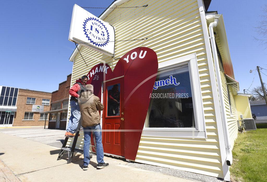 Tony Bertuca, owner of Hub 185 Central, and his son, Austin Bertuca, add names to a thank you heart sign framing the entrance to their restaurant Tuesday, April 21, 2020, in downtown Coloma, Mich. The restaurant is one of many who are only offering delivery and curbside pickup during the COVID-19 pandemic.(Don Campbell / The Herald-Palladium via AP)
