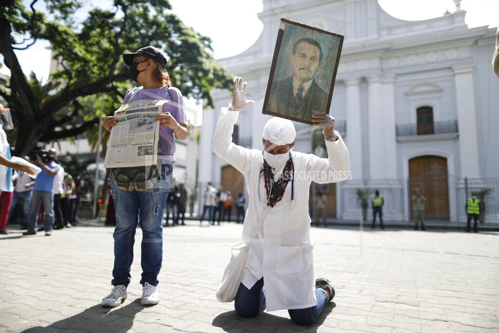 Ariana Cubillos Yeni Vasquez raises a portrait of the late, Venezuelan Dr. Jose Gregorio Hernandez outside the church in La Candelaria after the church bell rang, signaling the start of his Beatification ceremony in Caracas, Venezuela, Friday, April 30, 2021. Known as the "doctor of the poor, Hernandez is being Beatified by the Catholic church, a step towards sainthood. (AP Photo/Ariana Cubillos)
