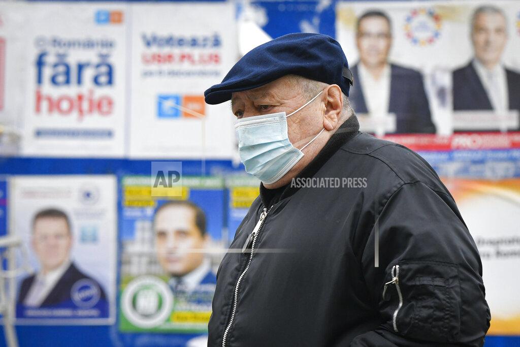 Andreea Alexandru A man wearing a mask for protection against the COVID-19 infection walks by electoral posters in Bucharest, Romania, Thursday, Dec. 3, 2020. Romania will hold parliamentary elections on Sunday Dec. 6. (AP Photo/Andreea Alexandru)