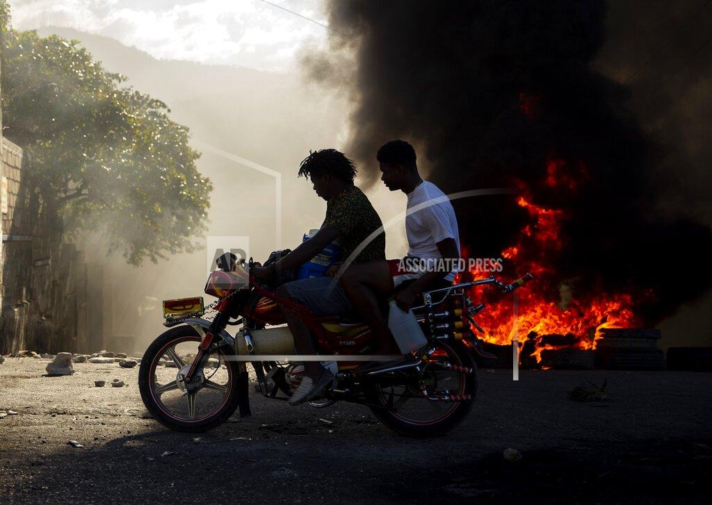 Dieu Nalio Chery Men ride a motorcycle past a burning barricade during a protest to demand the resignation of Haitian President Jovenel Moise in Port-au-Prince, Haiti, Sunday, Feb. 7, 2021. ( AP Photo/Dieu Nalio Chery)