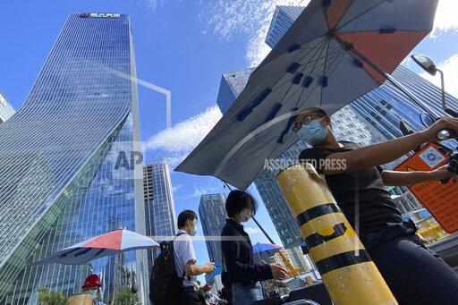 Men on electric bikes wait for riders near the Evergrande headquarters, left, in Shenzhen, China, Friday, Sept. 24, 2021. Seeking to dispel fears of financial turmoil, some Chinese banks are disclosing what they are owed by a real estate developer that is struggling under $310 billion in debt, saying they can cope with a potential default. (AP Photo/Ng Han Guan)