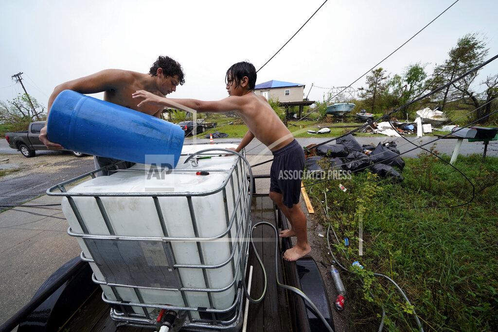 Gerald Herbert Terren Dardar, 17, left, and Dayton Verdin, 14, pour barrels of rainwater they collected from Tropical Storm Nicholas, in the aftermath of Hurricane Ida in Pointe-aux-Chenes, La., Tuesday, Sept. 14, 2021. They have had no running water since the hurricane, and collected 140 gallons of rainwater in two hours from the tropical storm, which they filter and pump into their house for showers. (AP Photo/Gerald Herbert)