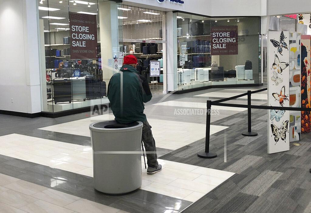 David Zalubowski A lone customer sits on the edge of a reeptacle near a store in which closing signs hang in the windows early Monday, Nov. 30, 2020, in an outlet mall in Lakewood, Colo. (AP Photo/David Zalubowski)
