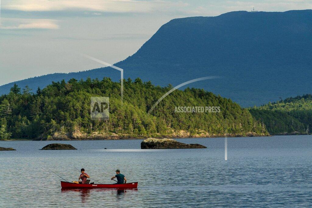 Robert F. Bukaty A man fishes from the bow of a canoe on Lobster Lake, Thursday, Aug. 13, 2020, in Lobster Township, Maine. Water levels in the lake are low this summer. The high water mark can be seen on the rock at center. (AP Photo/Robert F. Bukaty)