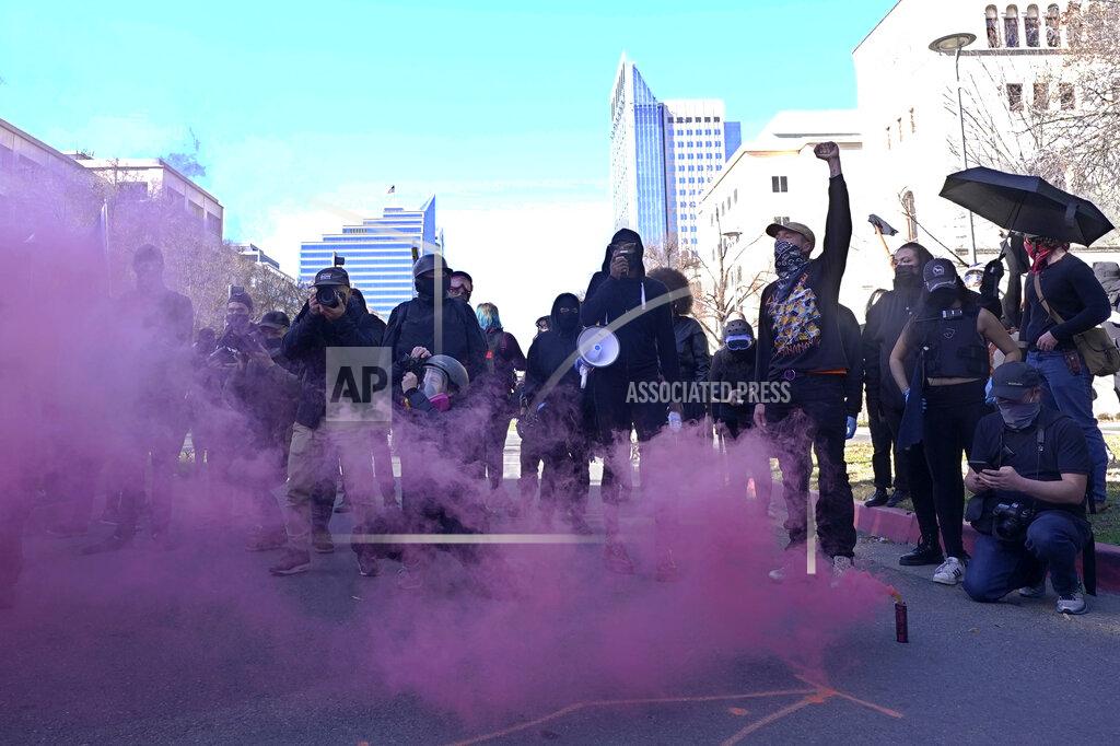 Rich Pedroncelli Black clad protesters set off a smoke bomb during a demonstration near the state Capitol in Sacramento, Calif., Wednesday, Jan. 20, 2021. Several dozen protesters marched through the downtown area to the Capitol where they were stopped at a temporary 6-foot high chain-link fence installed to stop violence on the Inauguration Day of President Joe Biden and Vice President Kamala Harris. (AP Photo/Rich Pedroncelli)