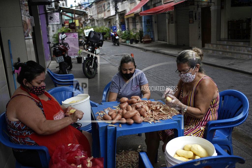 Silvia Izquierdo Women peel potatoes outside a snack bar amid the new coronavirus pandemic in Rio de Janeiro, Brazil, Friday, Oct. 9, 2020. Many people in Brazil are struggling to cope with less pandemic aid from the government and jumping food prices, with millions expected to slip back into poverty. (AP Photo/Silvia Izquierdo)