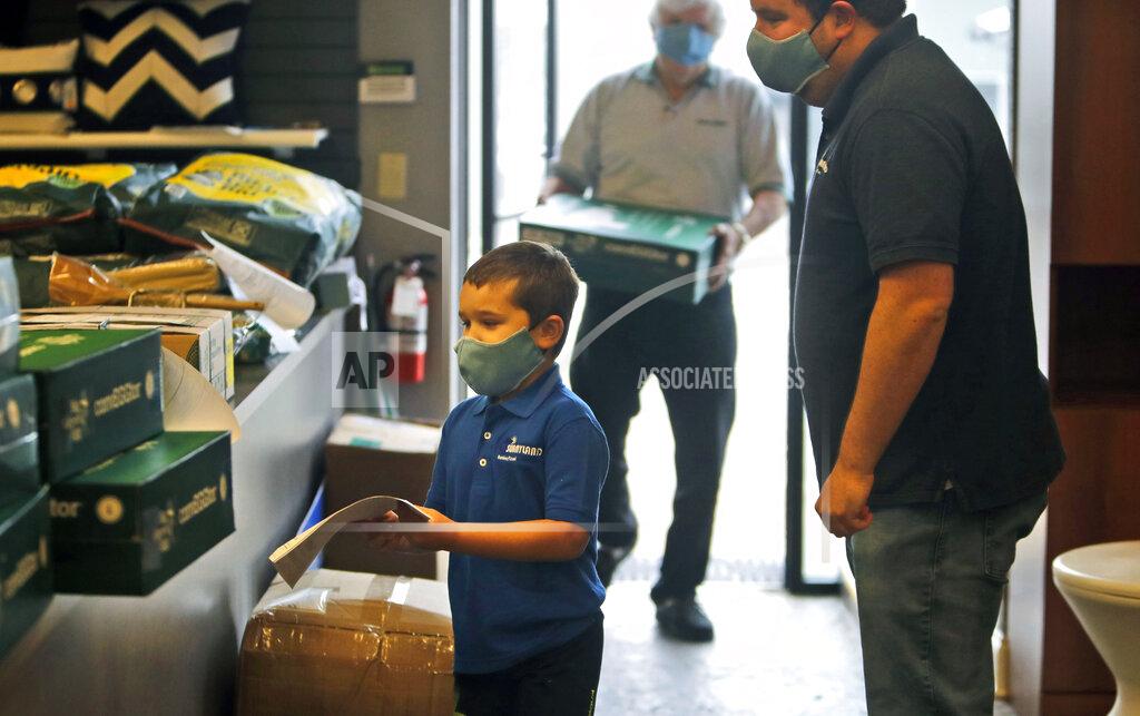 FILE - In this April 22, 2020 file photo, amid concerns of the spread of COVID-19, kindergartner Eli Schweig, 6, helps his father Brad Schweig, right, and grandfather David Schweig unload products as they prepare their family owned retail store Sunnyland Outdoor Living for a limited re-opening in Dallas. As small and midsize businesses rehire laid-off employees and get back to work, owners are making substantial changes to their operations to protect staffers from the coronavirus. (AP Photo/LM Otero, File)