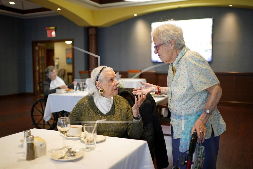 Seth Wenig FILE - Ita Aber, right, stops by the table of her old friend Rita Shliselberg after she finished dinner at RiverWalk, an independent senior housing facility, in New York, Thursday, April 1, 2021. Since the start of the pandemic, residents had been dining in their rooms. Only recently have they began to use the dining hall again. A focus on the elderly at the start of the nation's vaccination campaign helped protect nursing homes that were ravaged at the height of the U.S. coronavirus outbreak, but they are far from in the clear. New outbreaks, often traced to infected staff members, are still occurring in long-term care centers across the country, causing continued havoc for visitation policies. (AP Photo/Seth Wenig, File)