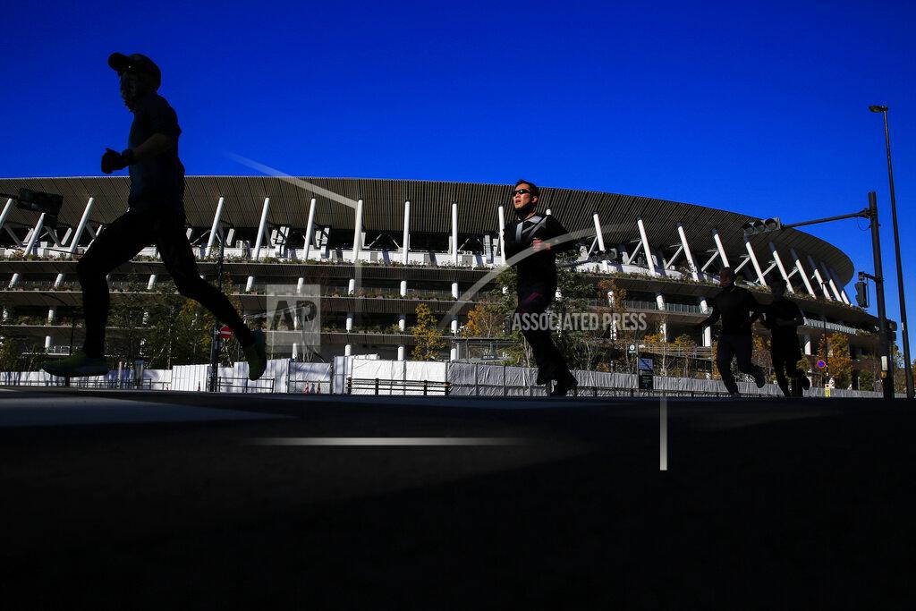 Kiichiro Sato Runners pass by Japan National Stadium, where opening ceremony and many other events are planned for postponed Tokyo 2020 Olympics, Thursday, Jan. 21, 2021, in Tokyo. The postponed Tokyo Olympics are to open in just six months. Local organizers and the International Olympic Committee say they will go ahead on July 23. But it’s still unclear how this will happen with virus cases surging in Tokyo and elsewhere around the globe. (AP Photo/Kiichiro Sato)