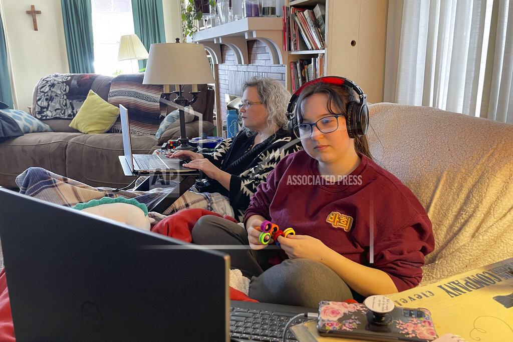Carolyn Thompson Angelina Mistretta, a 16-year-old junior at City Honors High School, shares the couch with her mother Wendy Mistretta, in Buffalo, N.Y., Feb. 17, 2021. Angelina Mistretta spins fidget toys as lessons stream through headphones, keeping her hands busy in hopes her mind will engage, too. (AP Photo/Carolyn Thompson)