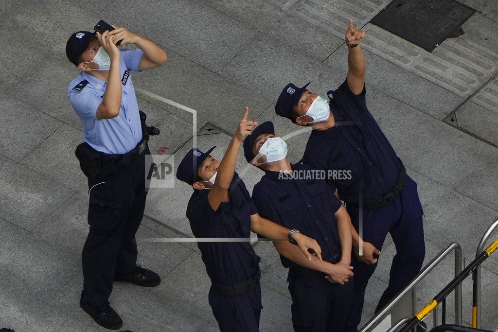 Ng Han Guan A police officer and security personnel react to something in the sky near the headquarters of the real estate developer Evergrande Group, Thursday, Sept. 23, 2021, in Shenzhen, southern China. Fears that the developer's possible default on multibillion-dollar debts might send shockwaves through global financial markets appeared to ease Thursday as creditors waited to see how much they might recover. (AP Photo/Ng Han Guan)