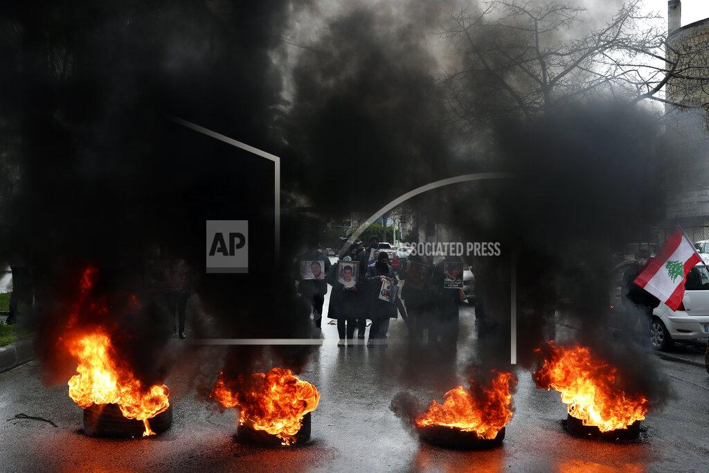 Bilal Hussein FILE - In this Feb. 19, 2021 file photo, relatives of victims of the Aug. 4, 2020 Beirut port explosion hold portraits of their loved one who were killed during the explosion, as they burn tires to block a road during a sit-in outside the Justice Palace, in Beirut, Lebanon. A public feud in recent weeks among prosecutors has starkly demonstrated how Lebanon's system of sectarian factions is paralyzing Lebanon's judicial system and snarling attempts to root out corruption. (AP Photo/Bilal Hussein, File)