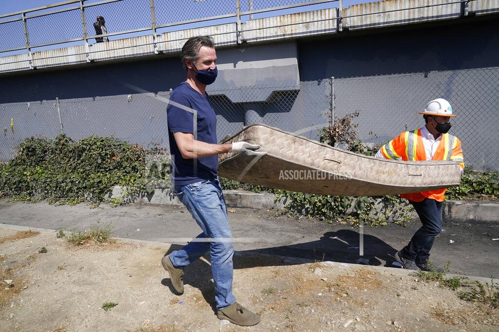 Marcio Jose Sanchez California Gov. Gavin Newsom, left, carries an old mattress as he joins a cleanup effort, Tuesday, May 11, 2021, in Los Angeles. Newsom on Tuesday proposed $12 billion in new funding to get more people experiencing homelessness in the state into housing and to "functionally end family homelessness" within five years. (AP Photo/Marcio Jose Sanchez)