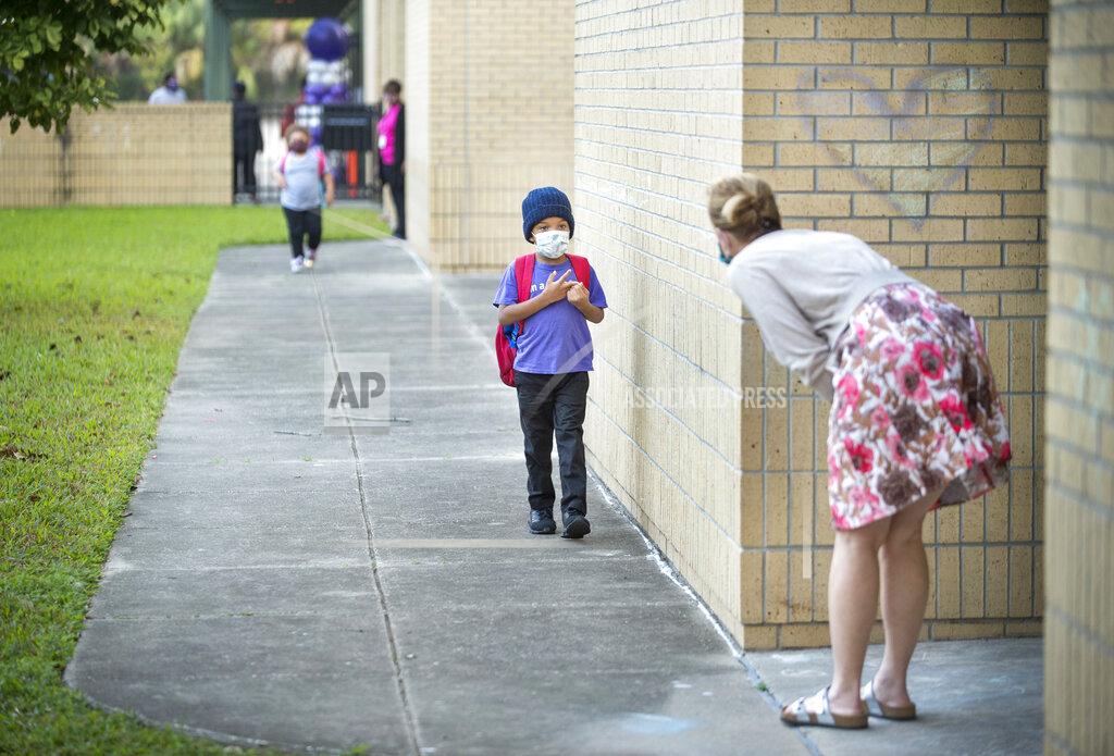 First grade teacher Bella Legault bends down to greet a nervous incoming student on the first day back at school for fifth-12th grade students at Foundation Preparatory School in New Orleans on Monday, Oct. 12, 2020. Because of coronavirus restrictions it was the first day of in-person learning for public school students in those grades in Orleans Parish. (Chris Granger/The Times-Picayune/The New Orleans Advocate via AP)
