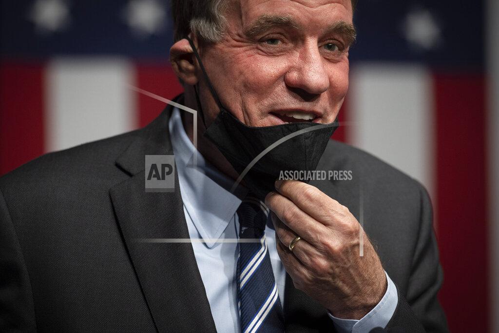 Cliff Owen Sen. Mark Warner, D-Va., adjusts his mask after addressing the news media about his Senate race against Daniel Gabe, on election night in Alexandria, Va., Tuesday, Nov. 3, 2020. (AP Photo/Cliff Owen)