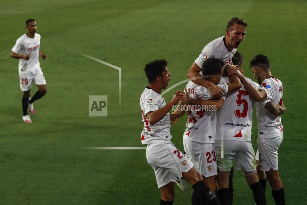 Str Sevilla's Lucas Ocampos, number 5, is congratulated after scoring against Betis during their Spanish La Liga soccer match in Seville, Spain, Thursday, June 11, 2020. With virtual crowds, daily matches and lots of testing for the coronavirus, soccer is coming back to Spain. The Spanish league resumes this week more than three months after it was suspended because of the pandemic, becoming the second top league to restart in Europe. The Bundesliga was first. The Premier League and the Italian league should be next in the coming weeks. (AP Photo)