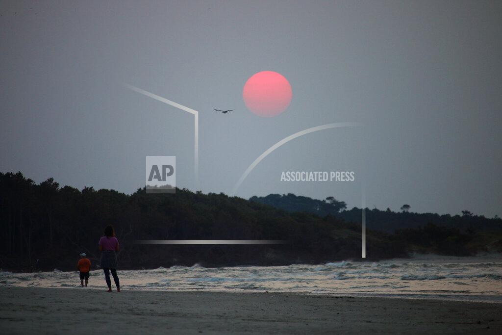 Mark Rogers A couple walks along the beach in Cherry Grove, S.C., early Thursday, July 22, 2021. Smoke from wildfires in the western U.S. and Canada is blanketing much of the continent, including thousands of miles away on the East Coast. And experts say the phenomenon is becoming more common as human-caused global warming stokes bigger and more intense blazes. (Mark Rogers/The Sanford Herald via AP)