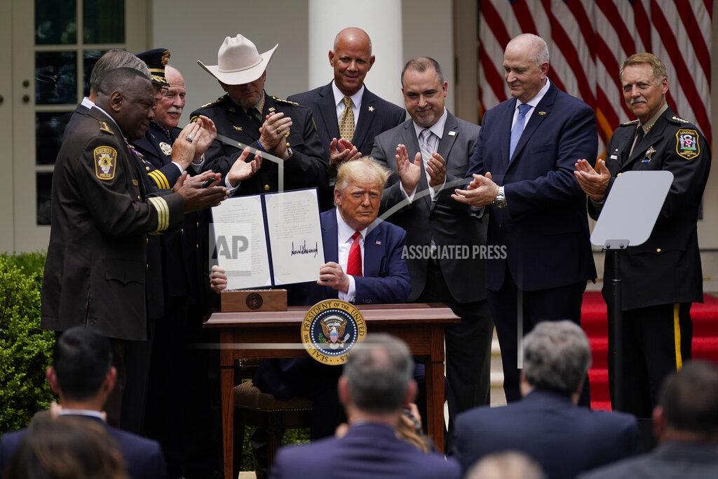 President Donald Trump holds up an executive order on police reform after signing it in the Rose Garden of the White House, Tuesday, June 16, 2020, in Washington. (AP Photo/Evan Vucci)