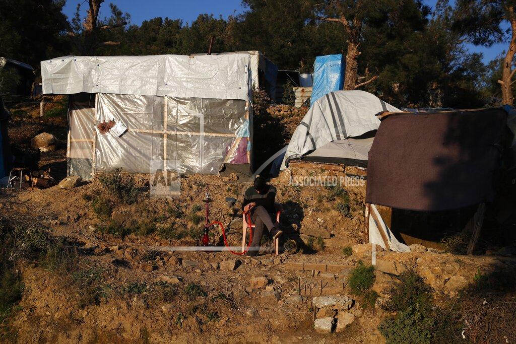 Thanassis Stavrakis A migrant sitting next to makeshift tents, smokes, outside the perimeter of the overcrowded refugee camp at the port of Vathy on the eastern Aegean island of Samos, Greece, Tuesday, Feb. 23, 2021. On a hill above a small island village, the sparkling blue of the Aegean just visible through the pine trees, lies a boy’s grave. His first ever boat ride was to be his last - the sea claimed him before his sixth birthday. His 25-year-old father, like so many before him, had hoped for a better life in Europe, far from the violence of his native Afghanistan. But his dreams were dashed on the rocks of Samos, a picturesque Greek island almost touching the Turkish coast. Still devastated from losing his only child, the father has now found himself charged with a felony count of child endangerment. (AP Photo/Thanassis Stavrakis)