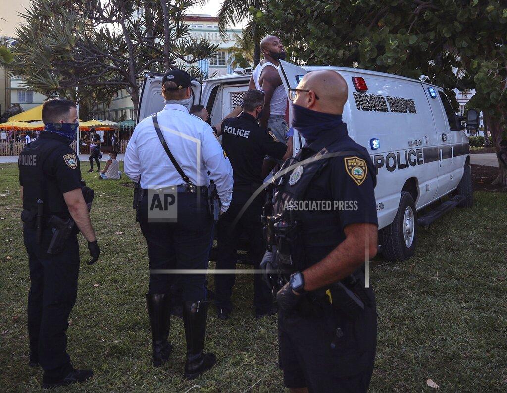 An unidentified man is detained and later arrested on Sunday, March 21, 2021, at 5th Street and Ocean Drive while crowds of Miami Beach spring-breakers walk Ocean Drive several hours prior to a city-wide curfew that was put into effect after several nights of mass arrests. An 8 p.m. curfew has been extended in Miami Beach after law enforcement worked to contain unruly crowds of spring break tourists (Carl Juste/Miami Herald via AP)