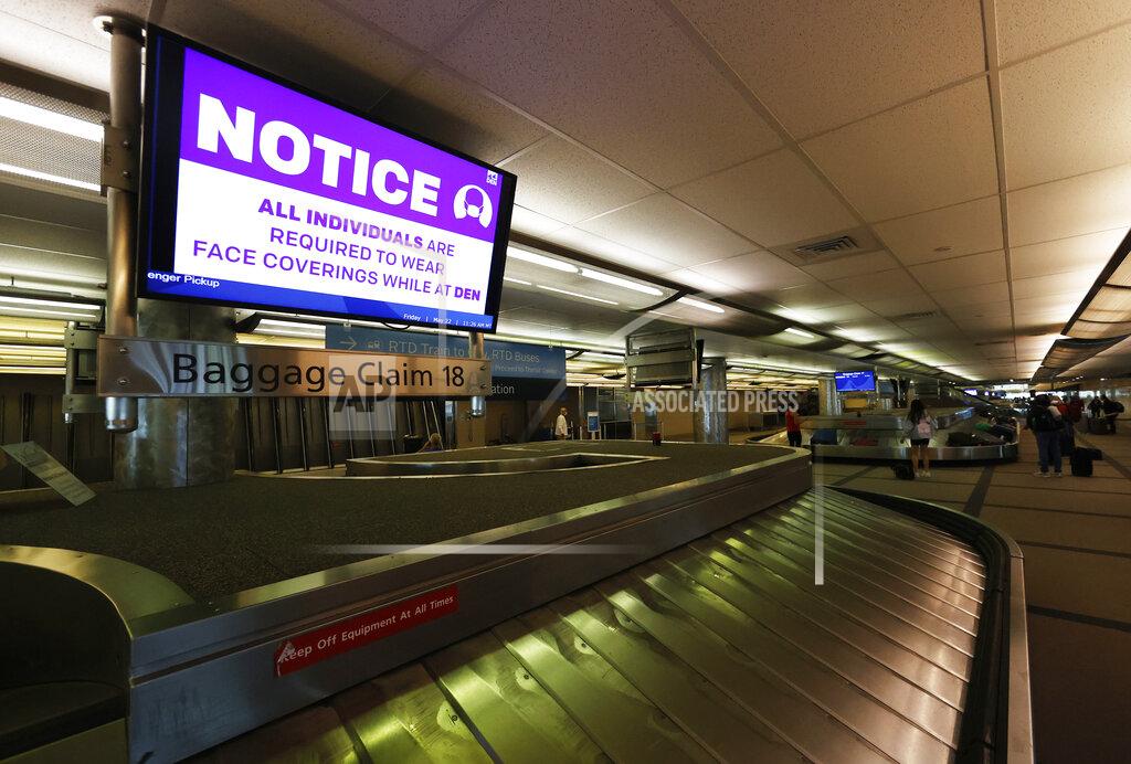 FILE - In this May 22, 2020 file photo, a message to wear a face mask flashes across a television monitor as travelers retrieve their bags off a carousel at Denver International Airport in Denver. Airlines are requiring passengers to wear masks, but recent incidents involving young children have put the carriers on the spot for how they enforce rules on face coverings. (AP Photo/David Zalubowski, File)