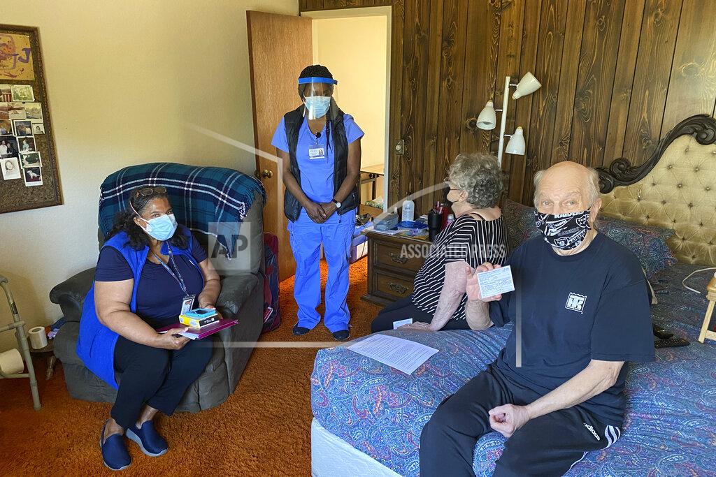 Terry Chea John McFarland, 70, shows his vaccination card after receiving the COVID-19 vaccine inside his bedroom in Hayward, Calif., May 6, 2021. Alameda County nurses Patricia Calloway, left, and Devette Laflore chat with his wife, Patti Amaral, 73, while they waited to make sure there were no vaccine side effects. (AP Photo/Terry Chea)