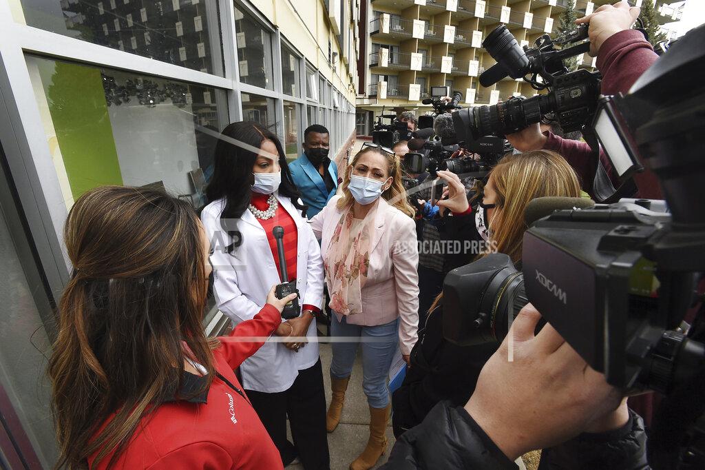 Dr. Sylvienash Moma, second from left, with hands clasped, declines to speak with the media, Monday, April 19, 2021, outside the Dr. Moma Health & Wellness Clinic at the Satellite Hotel in Colorado Springs, Colo., to address questions that the clinic allegedly improperly stored vaccines, prompting a state investigation. (Jerilee Bennett/The Gazette via AP)