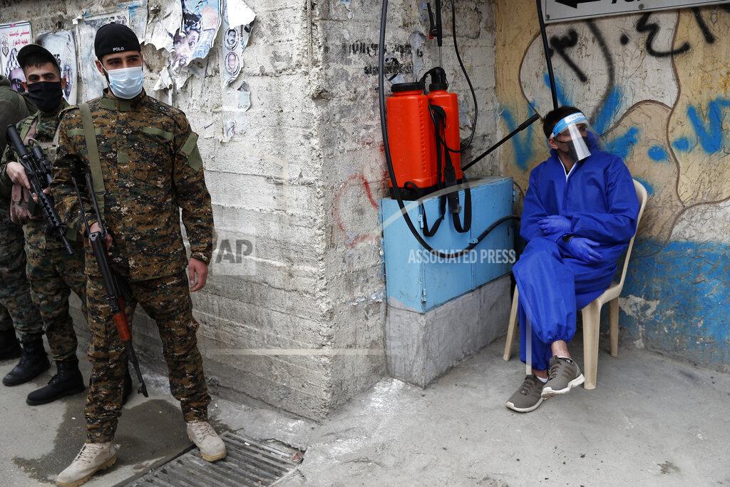 Hussein Malla Palestinian fighters from the Fatah movement, left, wearing masks to help curb the spread of the coronavirus, stand guard next to a Palestinian worker from UNRWA (United Nations Relief and works Agency), right, who is waiting to spray disinfectant at any car that need to enter inside Jalil, or Galilee refugee camp, in Baalbek, Lebanon, Friday, April 24, 2020. Authorities closed all entrances to a Palestinian refugee camp in eastern Lebanon Friday after four more people tested positive for the coronavirus, heightening concerns over the virus spreading among the population of overcrowded refugee camps and settlements. (AP Photo/Hussein Malla)