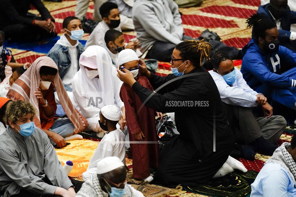 Matt Rourke A worshipper helps a child with a mask before he and others perform an Eid al-Fitr prayer at the Masjidullah Mosque in Philadelphia, Thursday, May 13, 2021. Millions of Muslims across the world are marking the holiday of Eid al-Fitr, the end of the fasting month of Ramadan. (AP Photo/Matt Rourke)