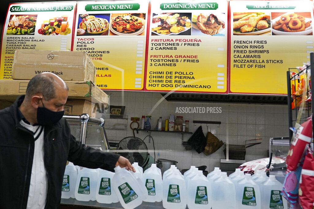 Kathy Willens Bodega owner Francisco Marte restocks his currently unused food service counter with water bottles, Wednesday, Feb. 10, 2021, in the Bronx borough of New York. Marte president of the Bodega and Small Business Group, which represents bodegas in New York, said he's been lobbying local officials to set aside COVID-19 vaccine appointments for bodega workers, many of whom are unaware they are eligible. He hopes that the recent opening of a large vaccination site at Yankee stadium will make access easier. (AP Photo/Kathy Willens)
