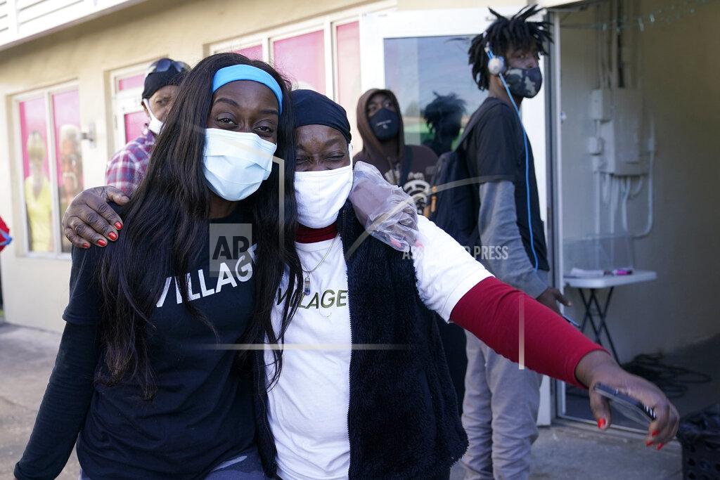 Lynne Sladky Sherina Jones, left, hugs her aunt Frances Jones, right, as a new community refrigerator she received with donations from friends is delivered, Wednesday, Dec. 9, 2020, in the Liberty City neighborhood of Miami. Jones offers free food for the community from a stocked community refrigerator called the Village Freedge. When one of the refrigerators was stolen just before Thanksgiving, the community and friends came together to help purchase a new one. Jones also provides hot food and distributes numerous food pantry items. She has applied for non-profit status and is transitioning to become a food bank. (AP Photo/Lynne Sladky)