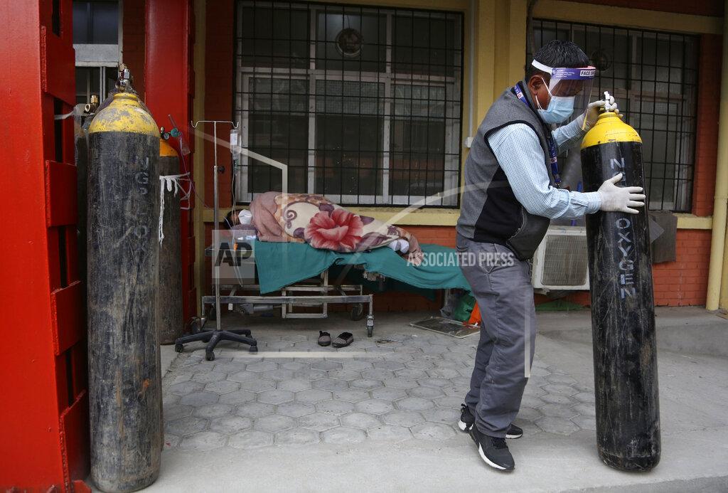 Niranjan Shrestha A Nepalese paramedic moves away an empty oxygen cylinder as a COVID-19 patient lies on a bed outside an emergency ward of a government run hospital in Kathmandu, Nepal, Friday, May 7, 2021. Across the border from a devastating surge in India, doctors in Nepal warned Friday of a major crisis as daily coronavirus cases hit a record and hospitals were running out of beds and oxygen. (AP Photo/Niranjan Shrestha)