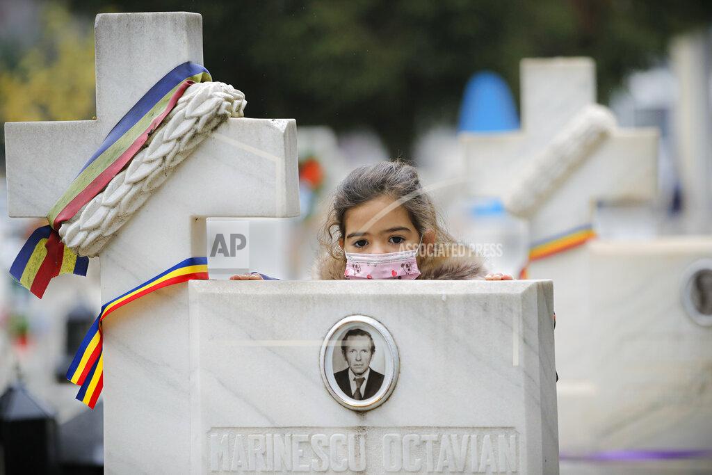 Vadim Ghirda A child, wearing a mask for protection against the COVID-19 infection, leans on the cross of a 1989 anti-communist revolution victim after a memorial religious service for those killed in the uprising, in Bucharest, Romania, Monday, Dec. 21, 2020. Participants and relatives of those killed marked the anniversary of the anti-communist uprising which started in Bucharest on Dec. 21, 1989, left more than one thousand people dead and ended the rule of dictator Nicolae Ceausescu. (AP Photo/Vadim Ghirda)