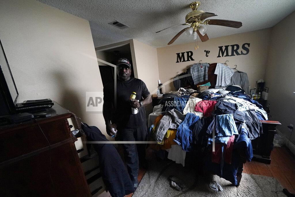 Gerald Herbert Michael Lathers carries his medicine from his bathroom past soaked clothes he spread on the bed to document for insurance in his flooded home, in the aftermath of Hurricane Ida in LaPlace, La., Tuesday, Sept. 7, 2021. (AP Photo/Gerald Herbert)