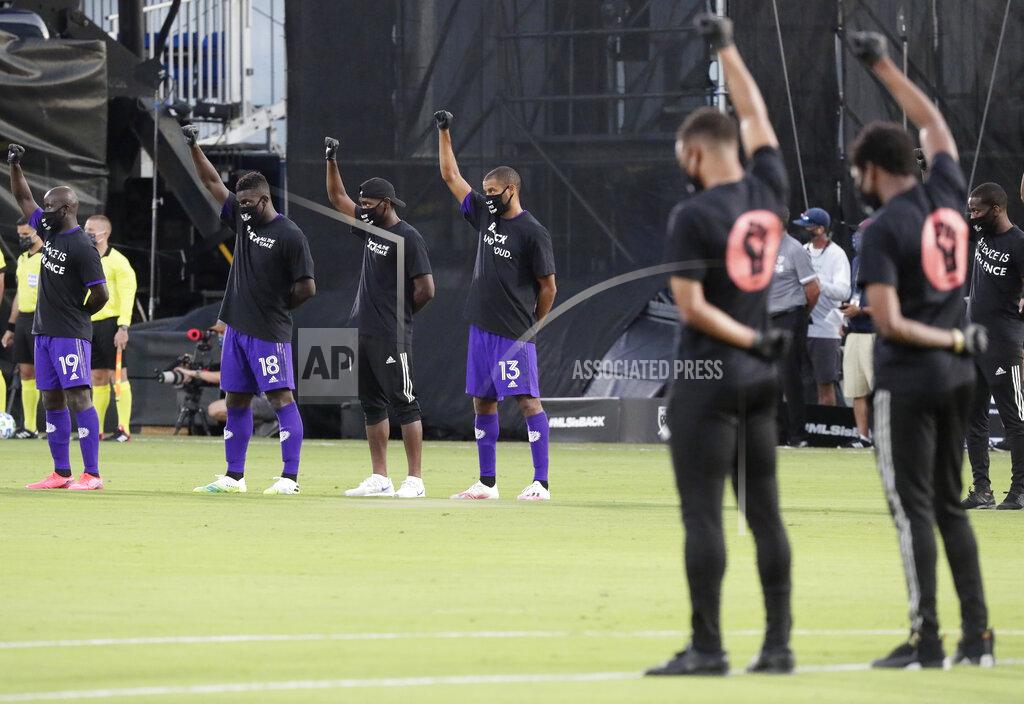 John Raoux Orlando City players, left, raise their fists in the air in solidarity with other MLS teams before the start of an MLS soccer match, Wednesday, July 8, 2020, in Kissimmee, Fla., while wearing shirts and masks with messages about race. (AP Photo/John Raoux)