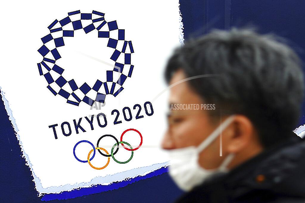 A man wearing a protective mask to help curb the spread of the coronavirus stands guard near a logo of Tokyo 2020 Olympic games in Tokyo on Feb. 1, 2021. Organizers and the International Olympic Committee pushed ahead Wednesday, April 28, 2021 with plans to open the postponed Tokyo Olympics in just under three months, unveiling the latest set of rule books to show how the games can be held during a pandemic. (AP Photo/Eugene Hoshiko)