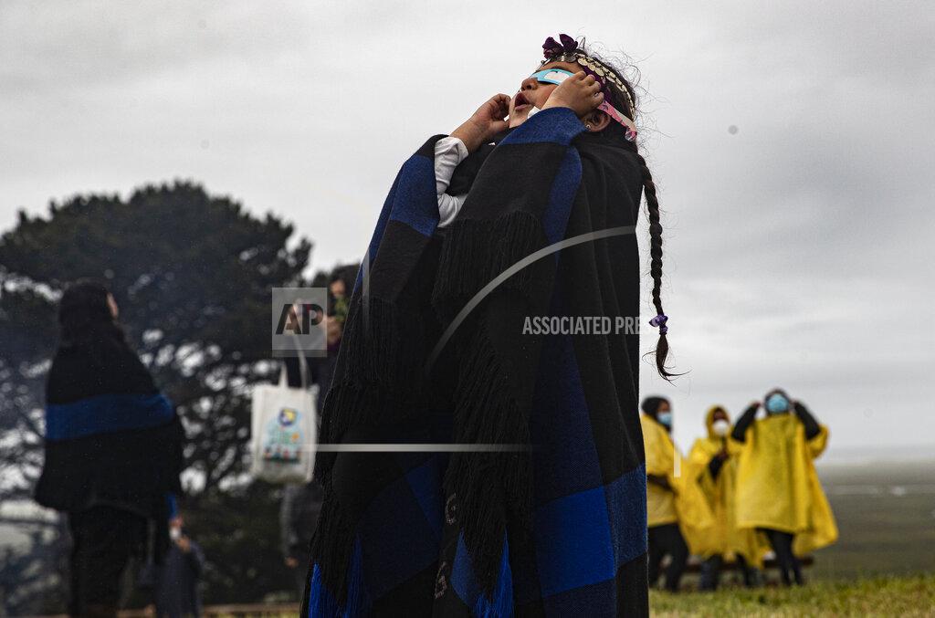 Esteban Felix Magdalena Nahuelpan, a Mapuche Indigenous girl, looks at a total solar eclipse through an overcast sky using special paper and plastic glasses in Carahue, La Araucania, Chile, Monday, Dec. 14, 2020. The total eclipse was visible from Chile and the northern Patagonia region of Argentina, and as a partial solar eclipse in Bolivia, Brazil, Ecuador, Paraguay, Peru and Uruguay. (AP Photo/Esteban Felix)