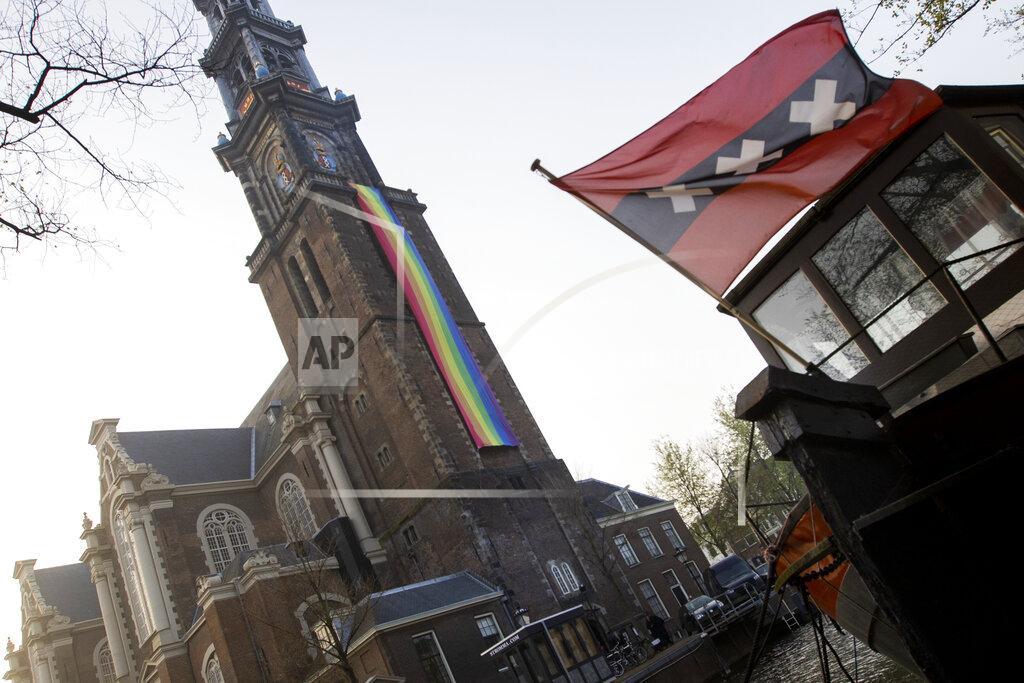Peter Dejong A large rainbow flag flies from the bell tower of Wester Church to mark the 20th anniversary of the first legalized same-sex marriage in Amsterdam, Netherlands, Thursday, April 1, 2021. Twenty years ago, the mayor of Amsterdam married four couples in City Hall as the Netherlands became the first country in the world with legalized same-sex marriage. It's now legal in 28 countries. The three crosses of the coat of arms of the city of Amsterdam are seen on a houseboat at right. (AP Photo/Peter Dejong)