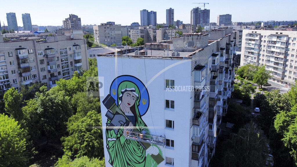 Natacha Pisarenko A worker paints a "Saint Javelin", a Virgin Mary holding an American-made anti-tank missile, in Kyiv, Ukraine, Tuesday, May 24, 2022. No matter where they live, the 3-month-old war never seems to be far away for Ukrainians. Those in towns and villages near the front lines hide in basements from constant shelling, struggling to survive with no electricity or gas — and often no running water. But even in regions out of the range of the heavy guns, frequent air raid sirens wail as a constant reminder that a Russian missile can strike at any time — even for those walking their dogs, riding their bicycles and taking their children to parks in cities like Kyiv, Kharkiv, Odesa and Lviv.(AP Photo/Natacha Pisarenko)