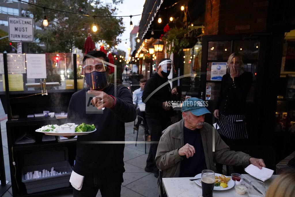 A server carries food for a customer at Ye Olde King's Head on Thursday, Nov. 19, 2020, in Santa Monica, Calif. The British restaurant and bar in seaside Southern California has been battered the past nine months and was in the process of adapting to new restrictions that took effect Friday, Nov. 20 that would further crimp its recovery even as the prospect of a crippling shutdown loomed. (AP Photo/Marcio Jose Sanchez)