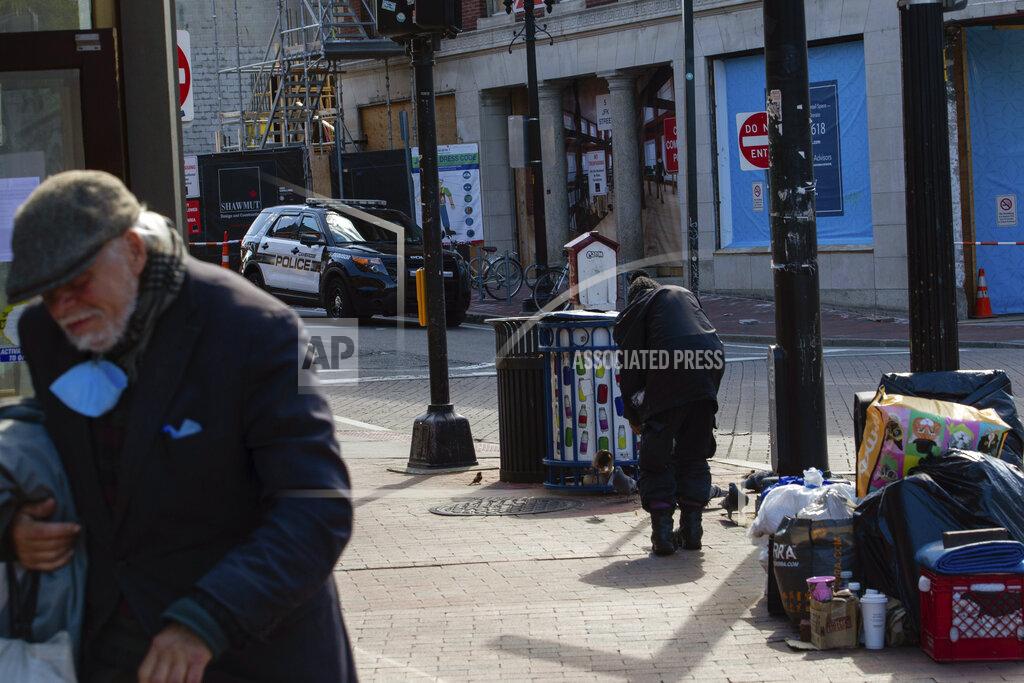 Sophie Park In this May 5, 2020 photo provided by Boston University via the Howard Center for Investigative Journalism, as a Cambridge, Mass., police officer watches from his car, a homeless man feeds the pigeons in Harvard Square amid the coronavirus pandemic. (Sophie Park/Boston University via AP)