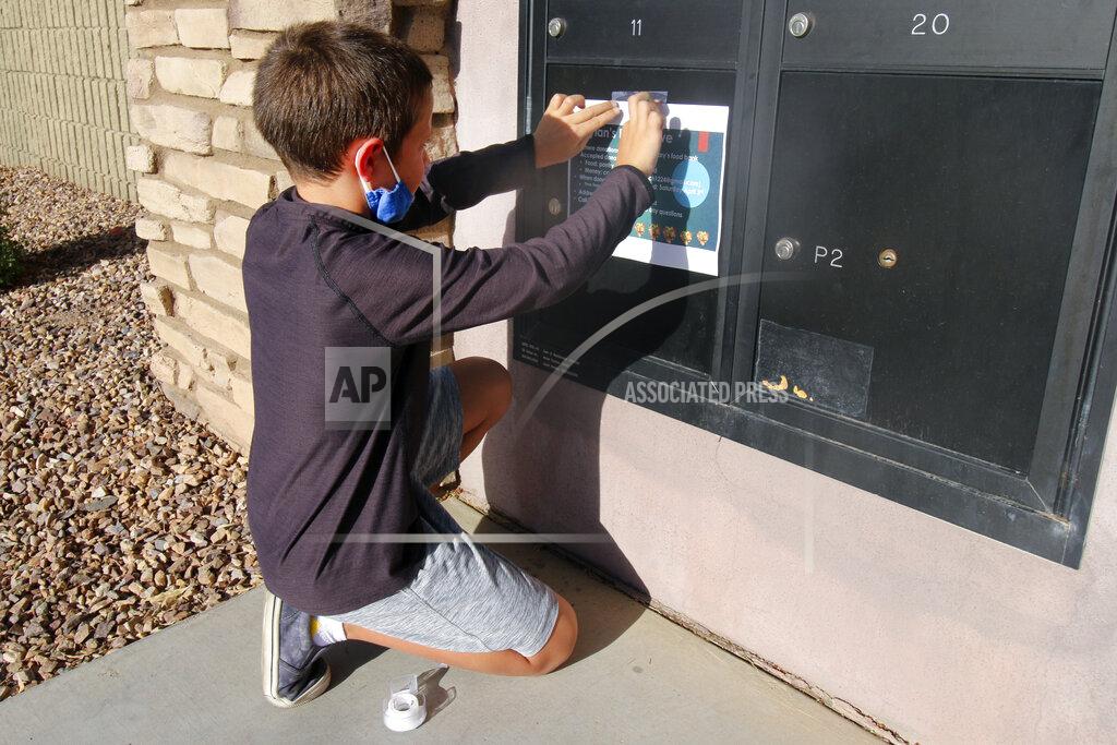 Cheyanne Mumphrey Dylan Pfeifer, 8, tapes up flyers in his neighborhood in Chandler, Ariz. on Thursday, April 1, 2021. The flyers promoted his third food drive since October in response to the coronavirus pandemic. (AP Photo/Cheyanne Mumphrey)